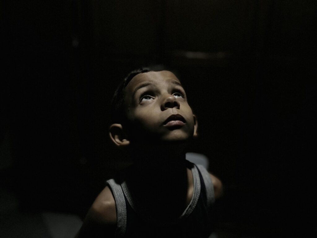 Portrait of a child looking up, seemingly contemplative, in a dimly lit environment.