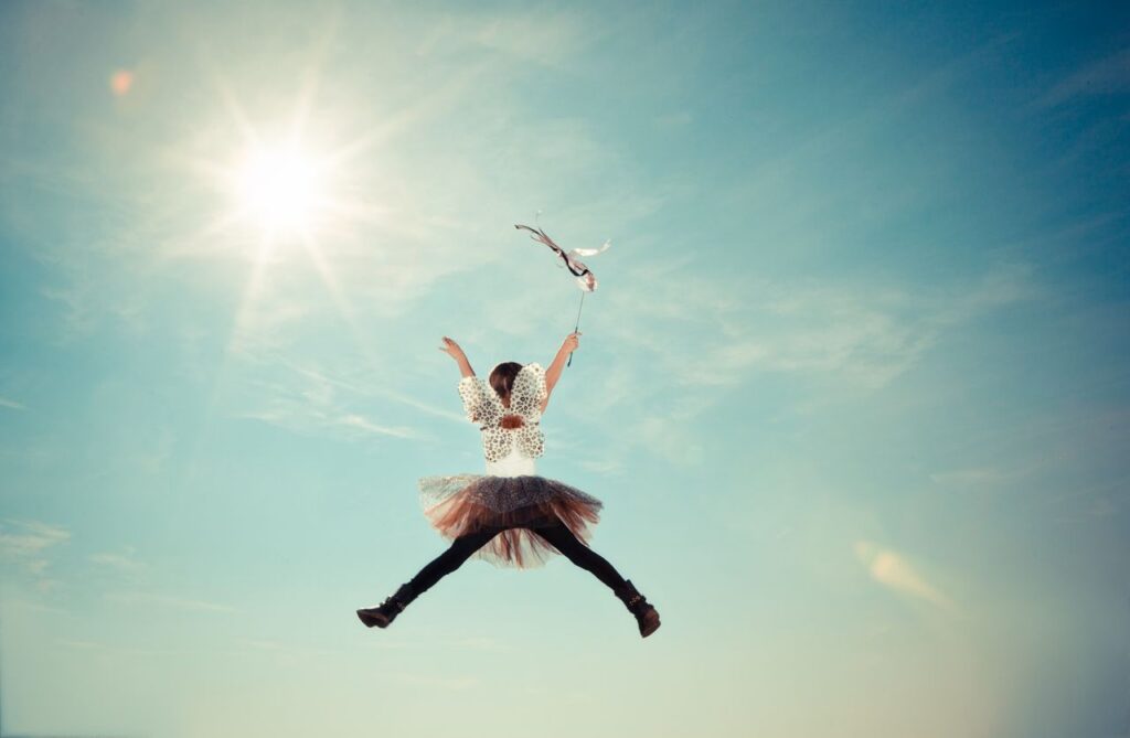 A young girl joyfully leaps in a fairy costume under the bright sun, capturing a moment of freedom and whimsy.
