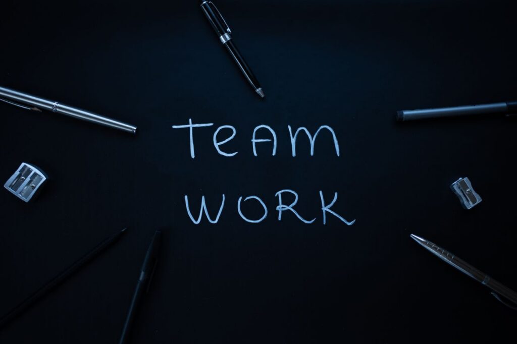 Arrangement of office supplies around teamwork text on black background.