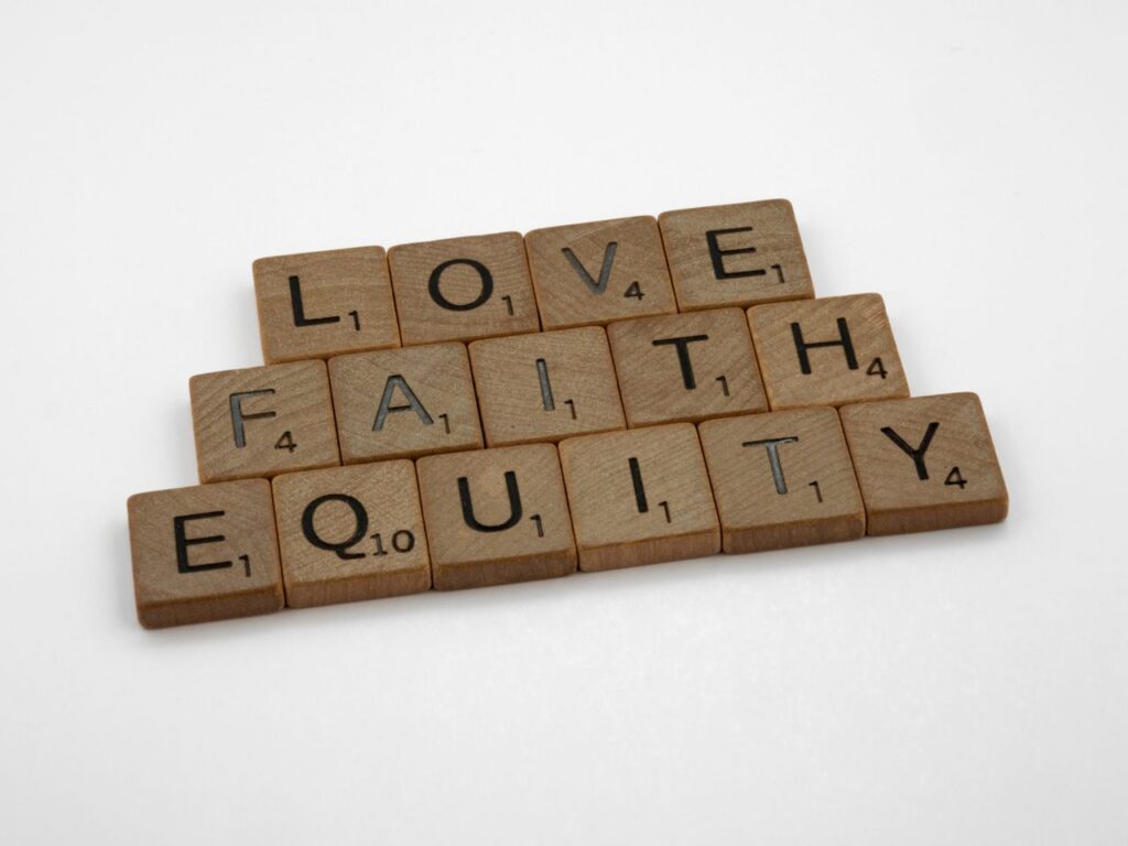 Close-up of wooden Scrabble tiles spelling Love, Faith, and Equity on a white surface.