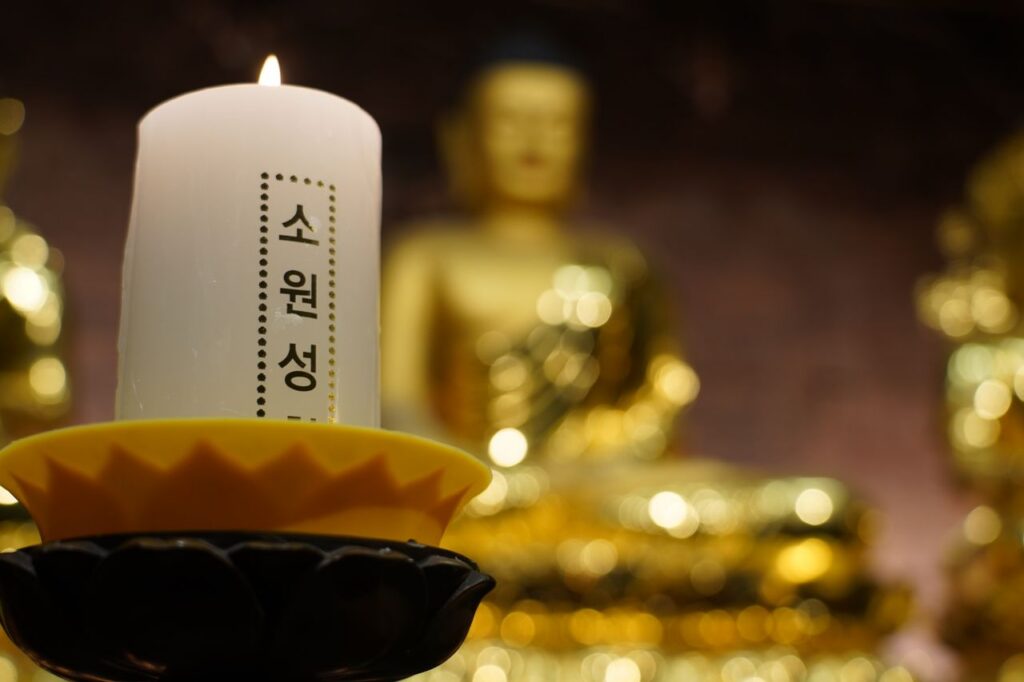 A lit candle with Korean text in front of a golden Buddha statue, Seoul temple.